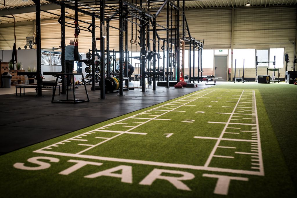 Indoor gym area with black floor mats, workout equipment, and a green turf track labeled "START" in white.